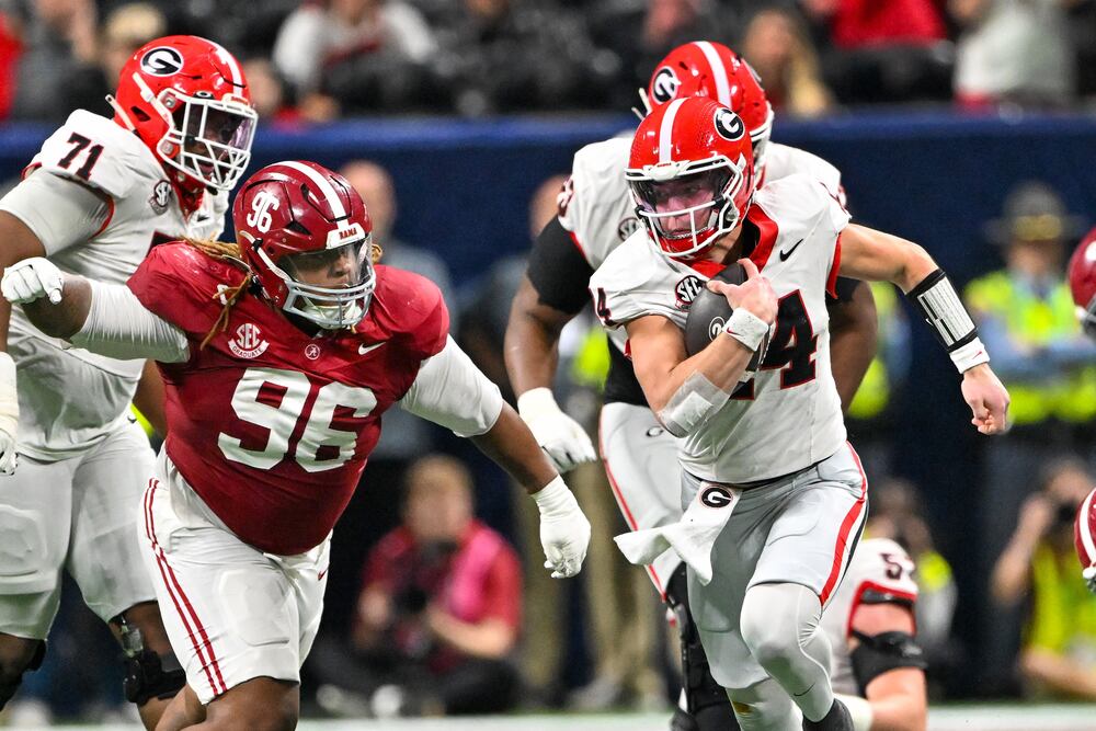 Georgia quarterback Gunner Stockton (right) runs past Alabama defensive lineman Tim Keenan III during the SEC championship game at Mercedes-Benz Stadium on Saturday, Dec. 6, 2025, in Atlanta. (Hyosub Shin/AJC)