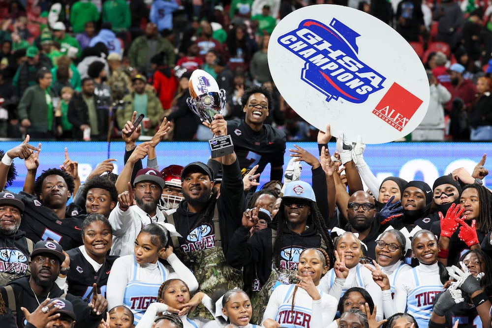 Carver-Columbus head coach Jarvis Jones hoists the trophy as Carver-Columbus celebrates their 24-7 win against Hapeville Charter in the Class 2A GHSA football championship at Mercedes-Benz Stadium, Tuesday, Dec. 16, 2025, in Atlanta. (Jason Getz/AJC)